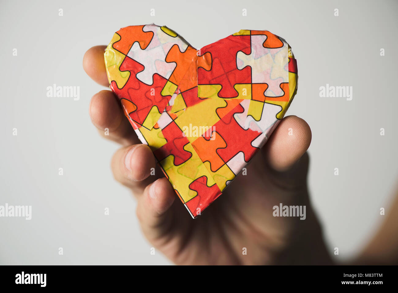 clousep of a young caucasian man holding a heart patterned with many puzzle pieces of different colors, symbol of the autism awareness Stock Photo