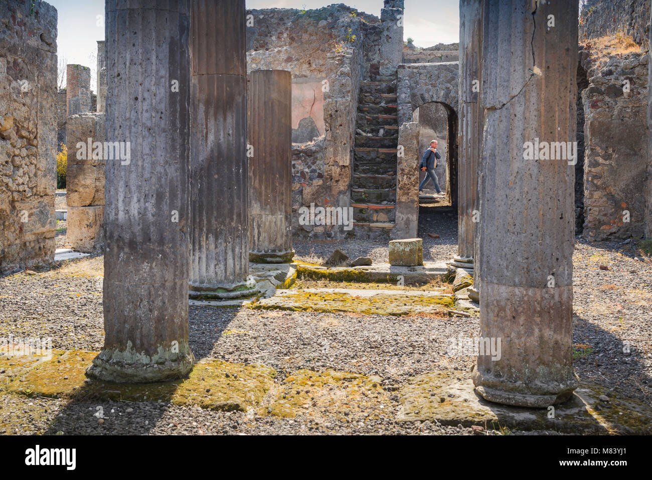 Pompeii ruins, view of the interior of an ancient Roman villa with a tourist walking by in the street outside the building, Bay of Naples, Italy. Stock Photo