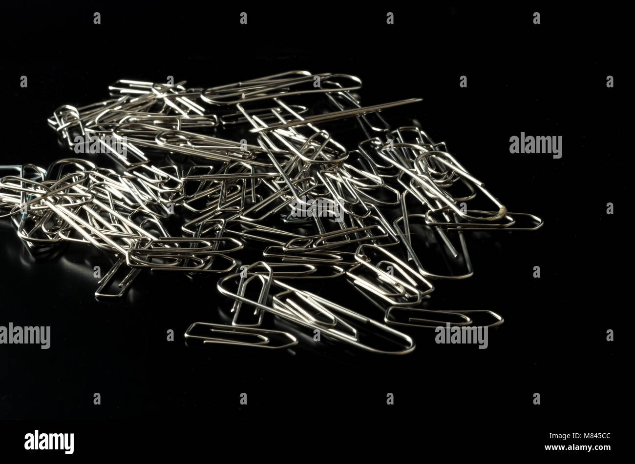Pile of metal paper clips on reflective black background Stock Photo