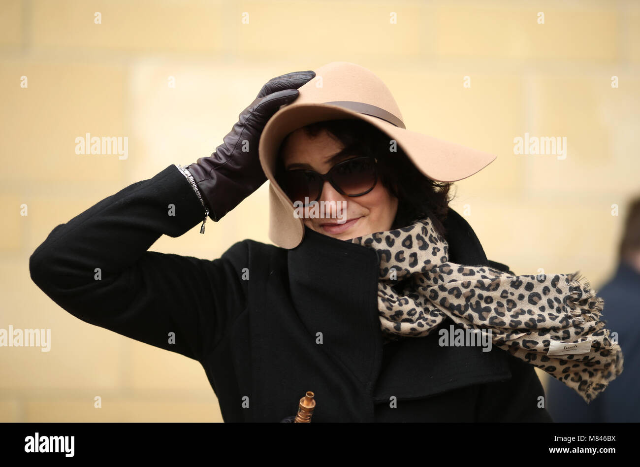 A female racegoer holds onto her hat during Ladies Day of the 2018 Cheltenham Festival at Cheltenham Racecourse. PRESS ASSOCIATION Photo. Picture date: Wednesday March 14, 2018. See PA story RACING Cheltenham. Photo credit should read: Steven Paston/PA Wire. RESTRICTIONS: Editorial Use only, commercial use is subject to prior permission from The Jockey Club/Cheltenham Racecourse. Stock Photo