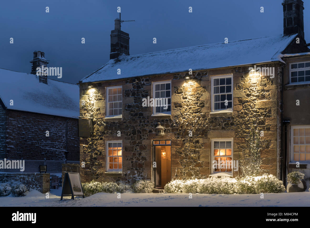Welcoming village inn on a snowy winter evening, Bamburgh, Northumberland, England. Winter (February) 2018. Stock Photo
