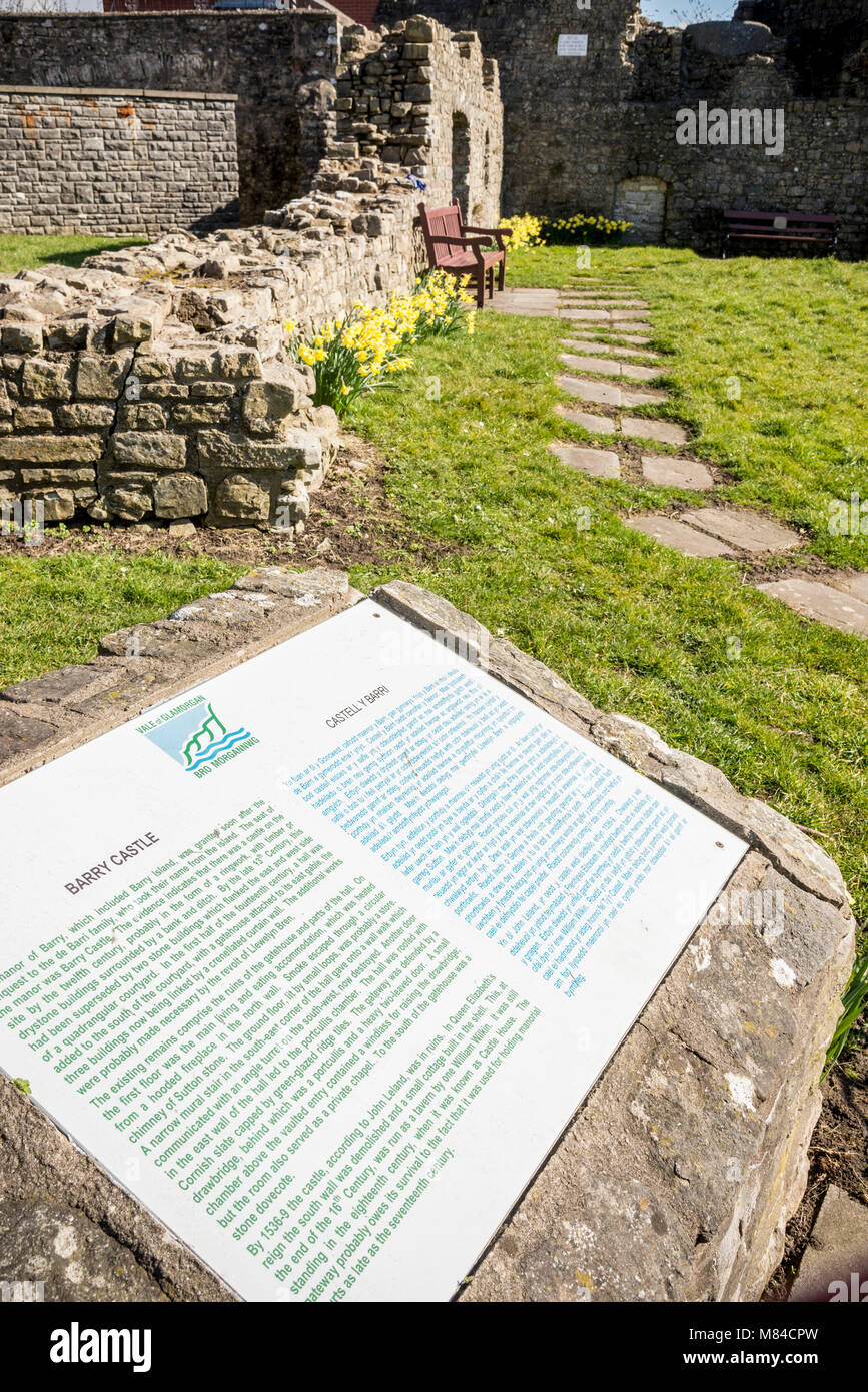 Bilingual, English and Welsh, tourist information sign in front of the sunlit ruins of Barry castle. Stock Photo