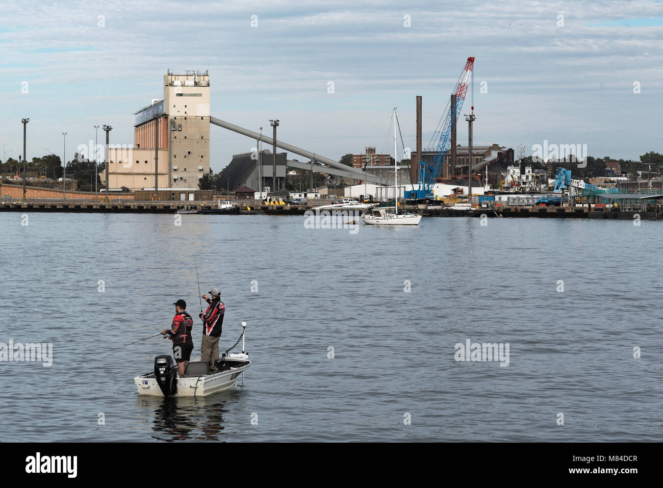 Two men fishing in a small boat (a Tinny) on Sydney harbour near White Bay. In the background is the Glebe Island silos that hold dry cement. Stock Photo