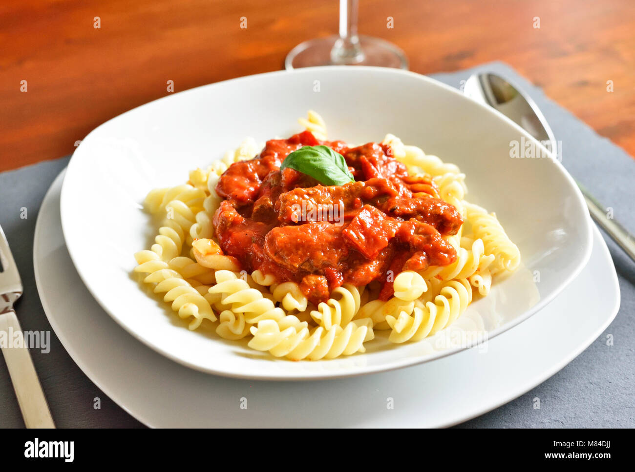 Delicious goulash dish on a white plate with basil leaf. Spiral pasta with tomato sauce. Stock Photo