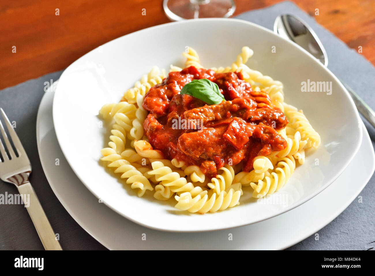 Delicious goulash dish on a white plate with basil leaf. Spiral pasta with tomato sauce. Stock Photo