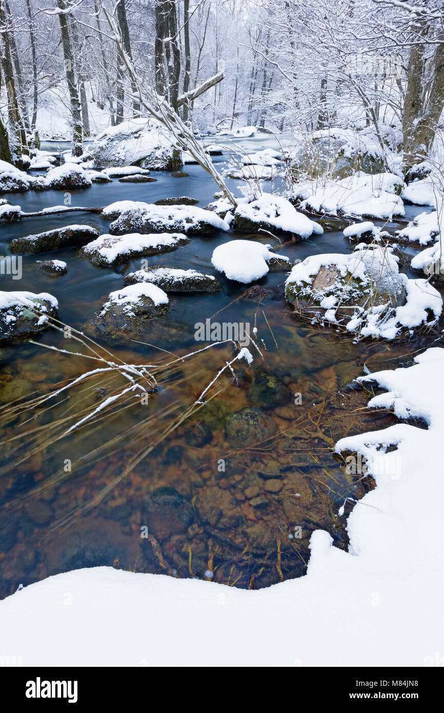 Long exposure low angle close up view river and river bed running through a frozen snow covered winter landscape view  Model Release: No. Property Release: No. Stock Photo