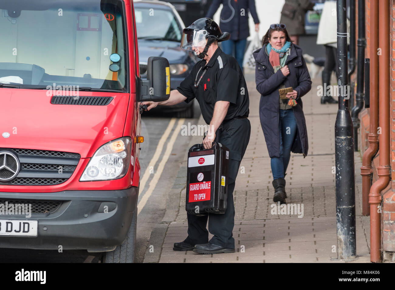 Male Post Office security guard in secure protective clothing carrying secure case to a van while delivering money to a Post Office in England, UK. Stock Photo