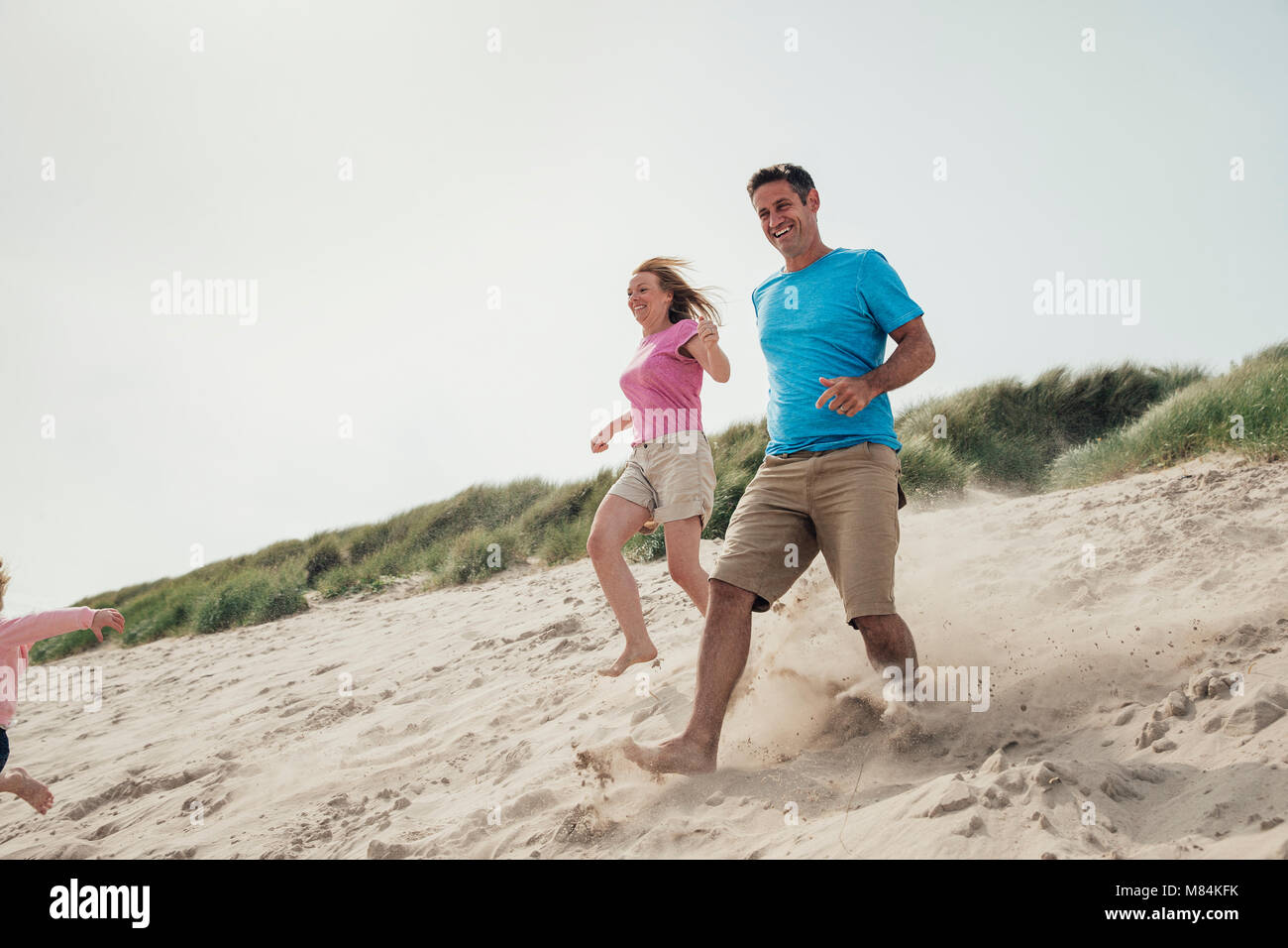 Low angle view of couple racing down a sand dune while on holiday at the seaside. Stock Photo