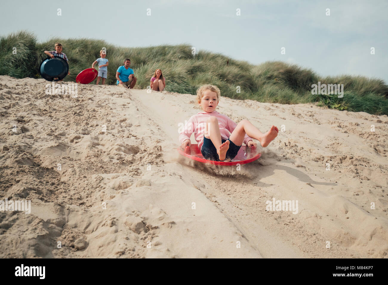 Little girl having fun, sliding down a sand dune while her family wait at the top Stock Photo