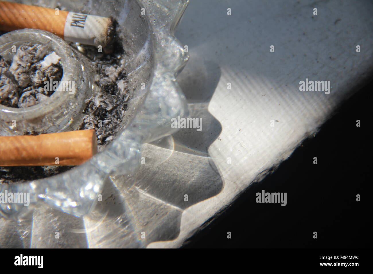 Cigarettes in a crystal ashtray on window sill. Stock Photo