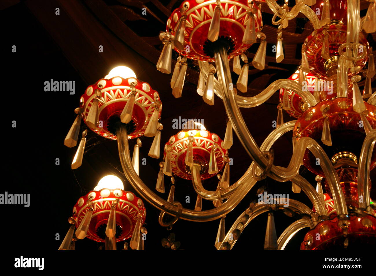 Beautiful crystal chandelier made of red glass is suspended from the ceiling. The lamps in the chandelier are on. Stock Photo