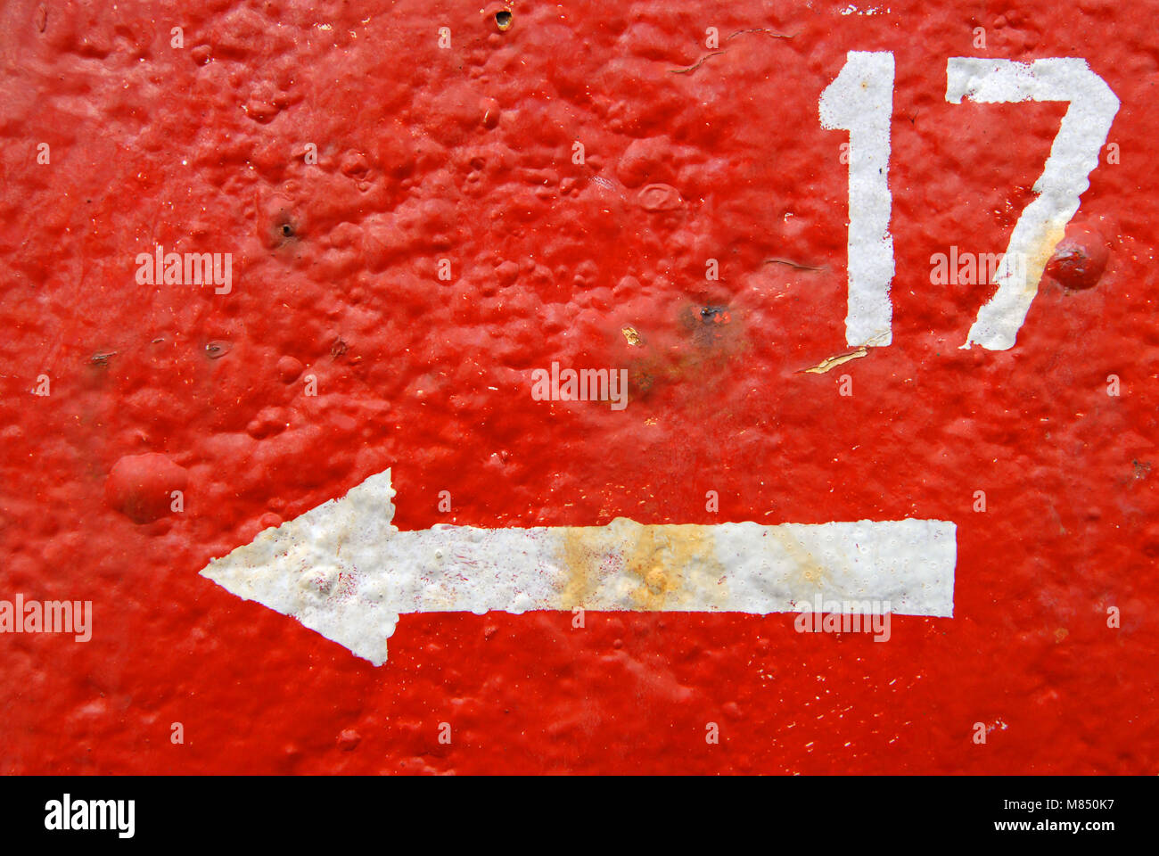 number 17 painted white on a rusty textured painted red background with an arrow pointing left Stock Photo