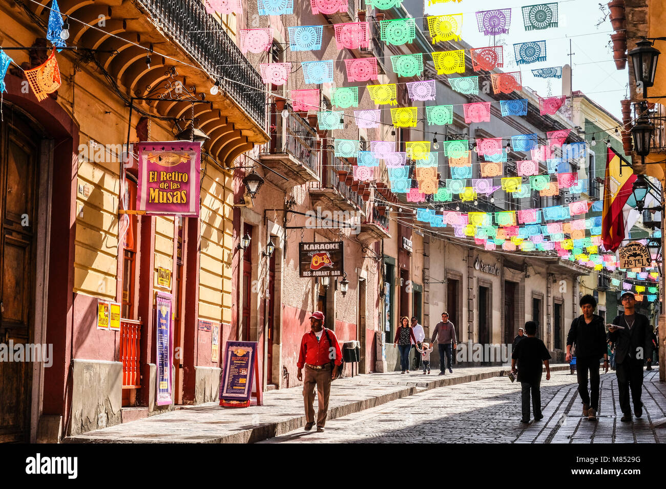Mexicans Walking On Cobblestone Street With Sun Lit Colorful