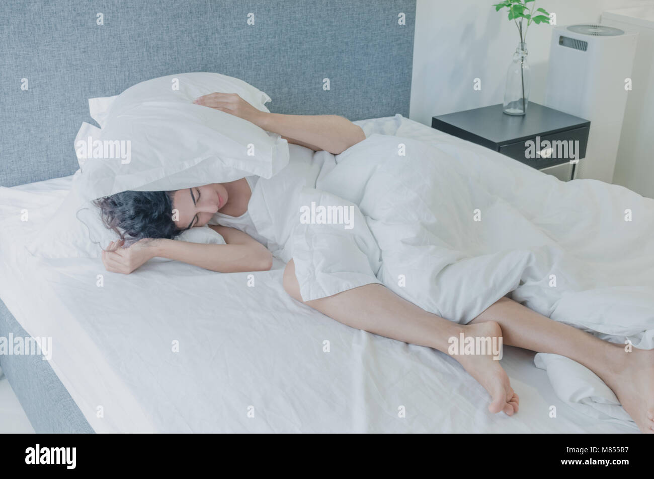 Young caucasian woman with black hair sleeps funny in bed, covering her