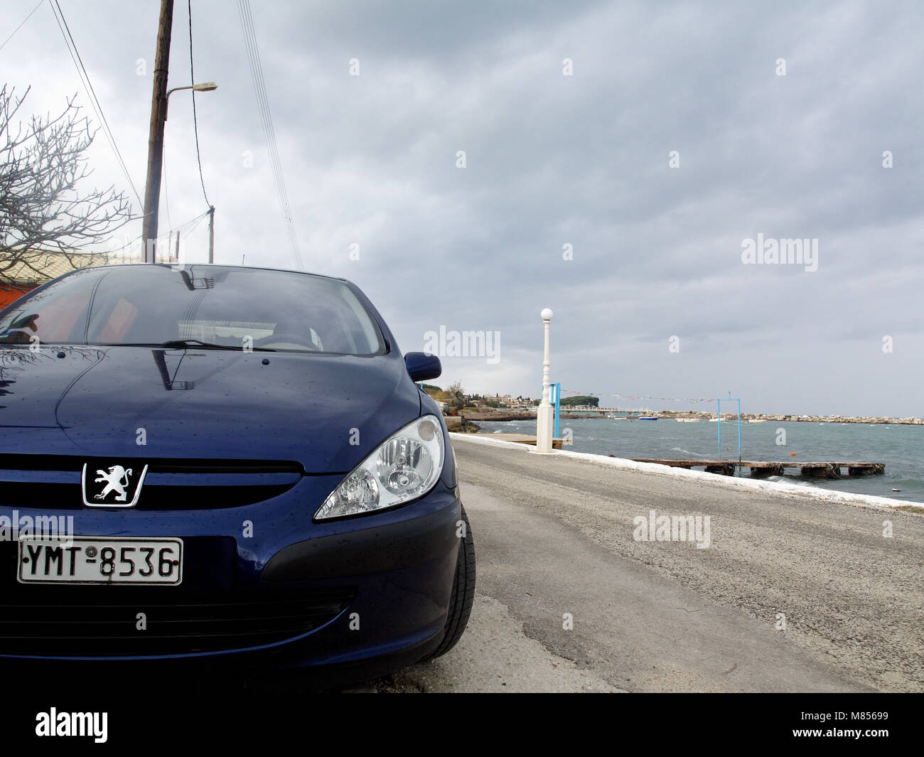 Blue Peugeot 307 parked near sea in Roda, Corfu, Greece on stormy winter day Stock Photo