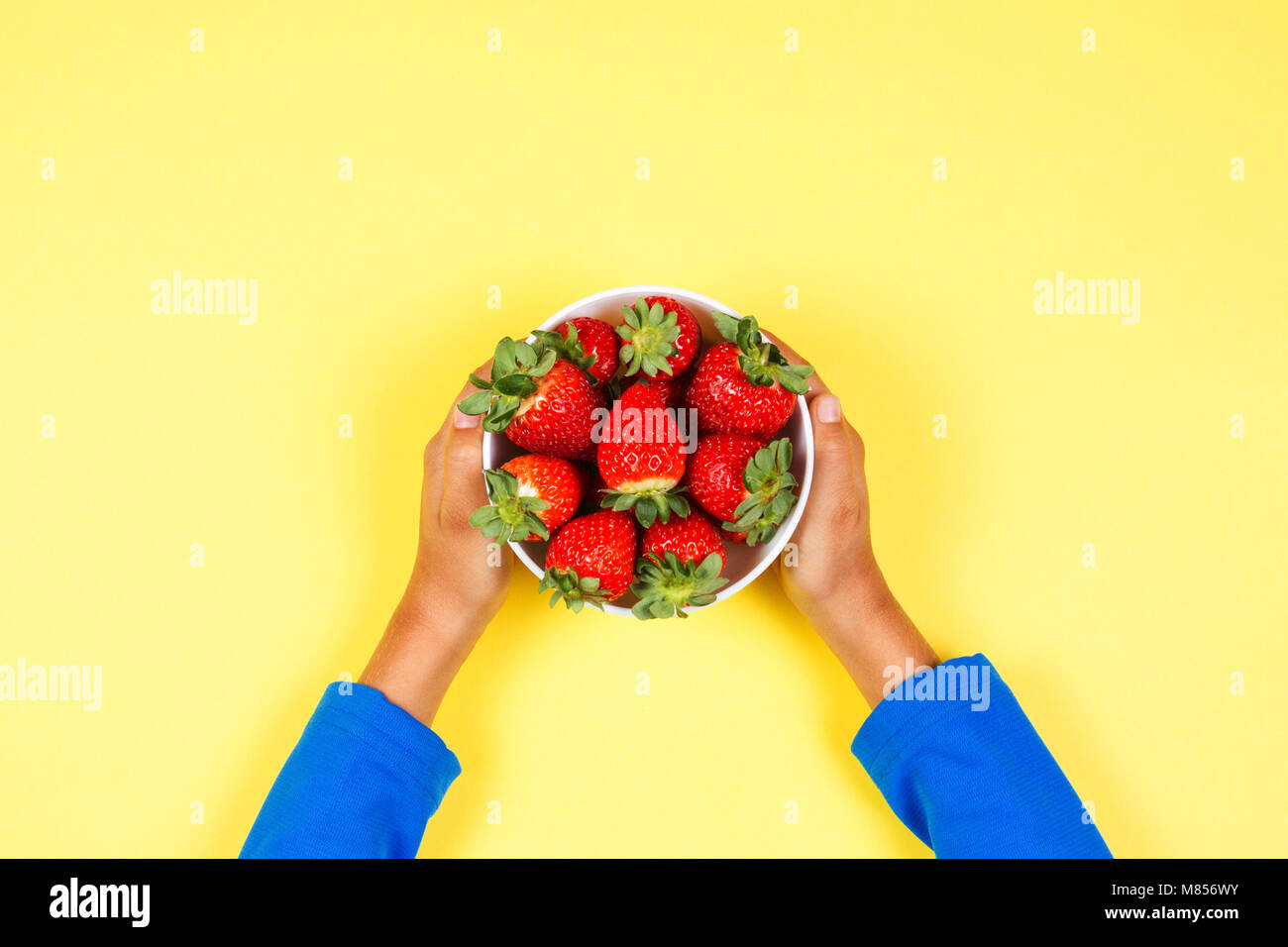 Kid holds in hand bowl with fresh strawberries on yellow background Stock Photo