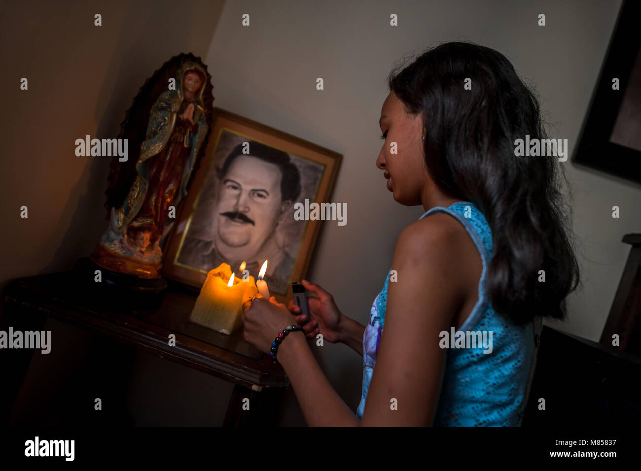 A Colombian girl lights up the candles at the altar of the drug lord Pablo Escobar, placed in the living room corner of a house in Medellín, Colombia. Stock Photo