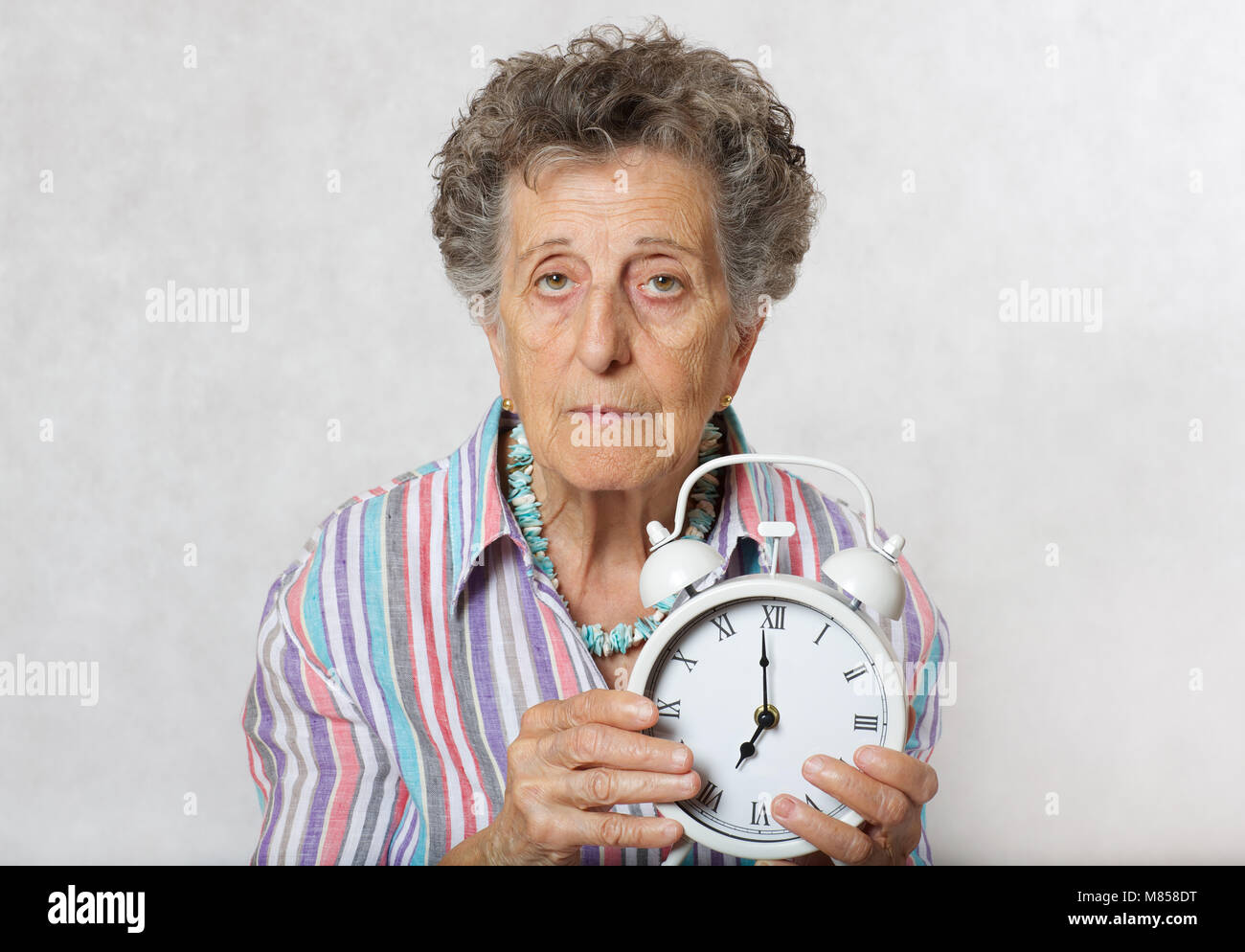 Senior woman between 70 and 80 years old shows vintage alarm clock Stock Photo Alamy