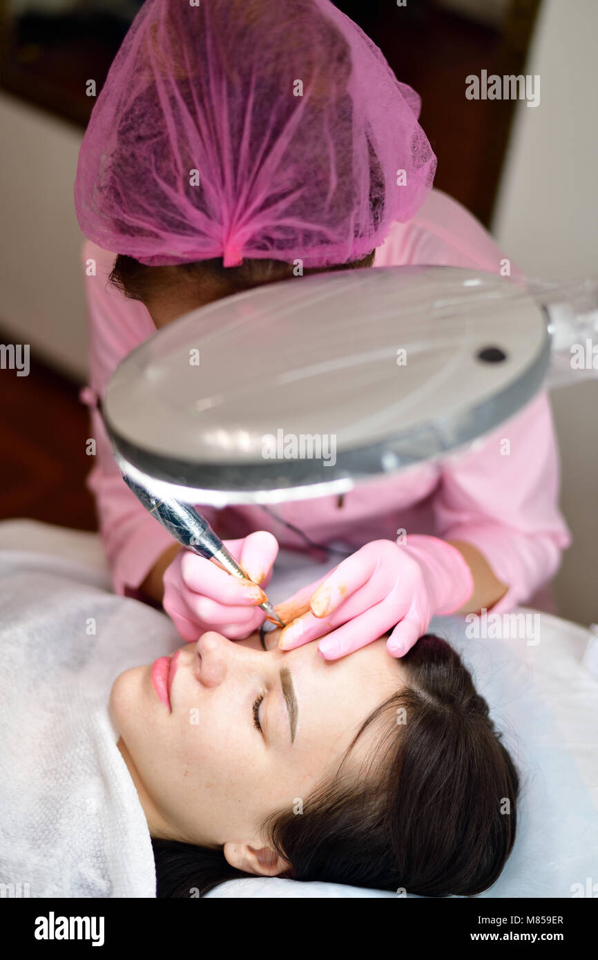 doctor cosmetologist doing instrumental coloring of eyebrows Stock Photo