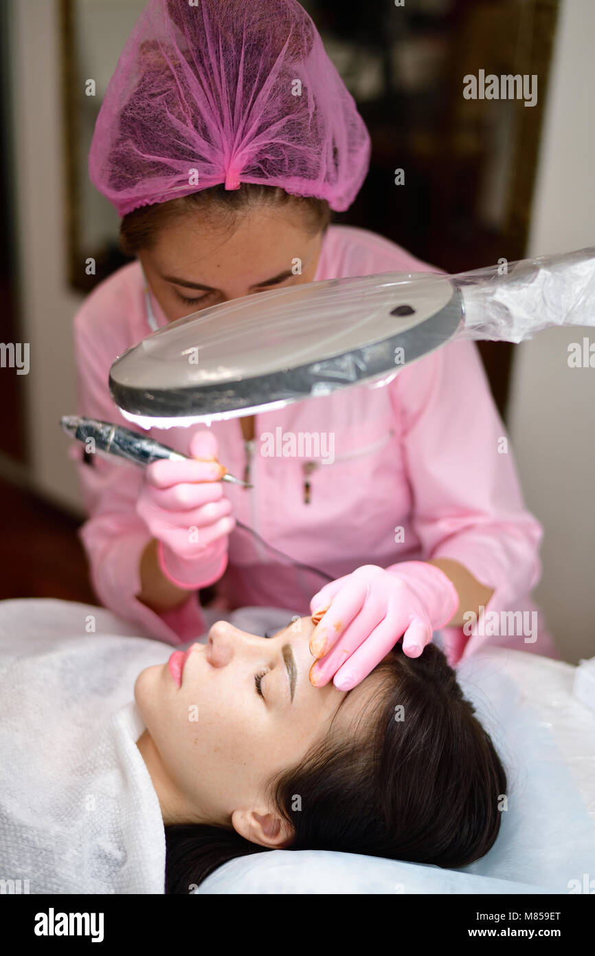 doctor cosmetologist doing instrumental coloring of eyebrows Stock Photo