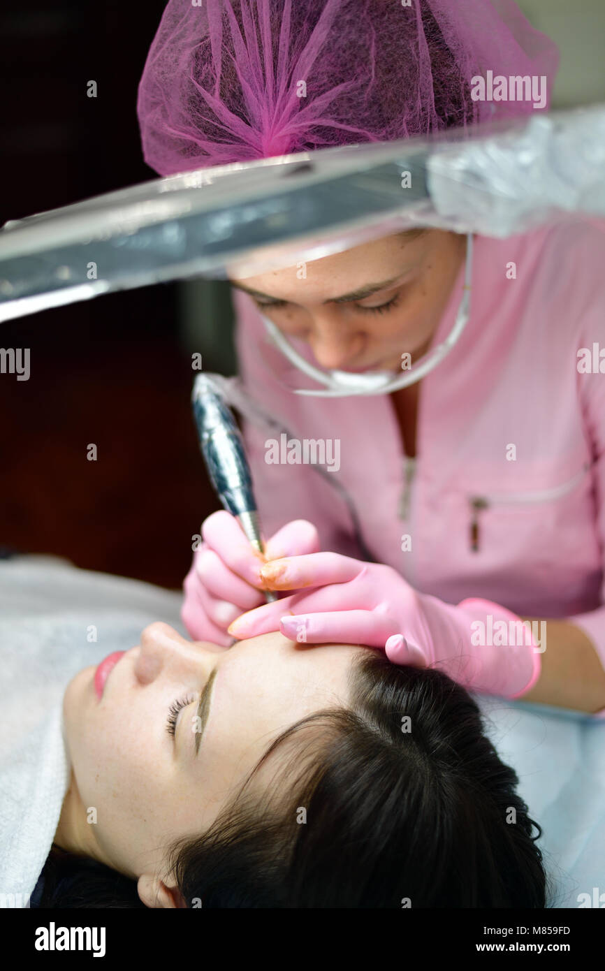 doctor cosmetologist doing machine coloring of eyebrows Stock Photo