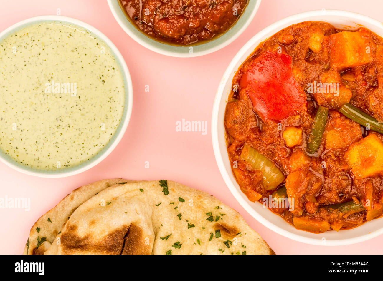 Indian Style Vegetarian Masala Curry Against A Pink Background With Dipping Sauces And Naan