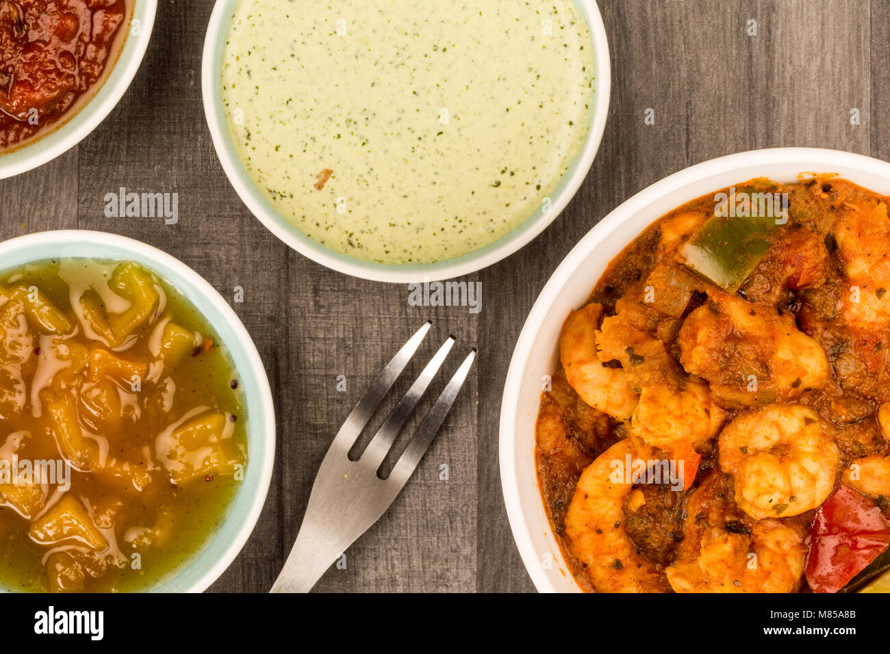 Spicy Indian Style King Prawn Bhuna Curry Against A Dark Wooden Kitchen Table Top With Dipping