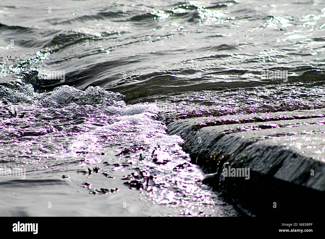 wave ripples falling over a slipway at dawn with the light shining through the bubbles. Ireland coastline Stock Photo
