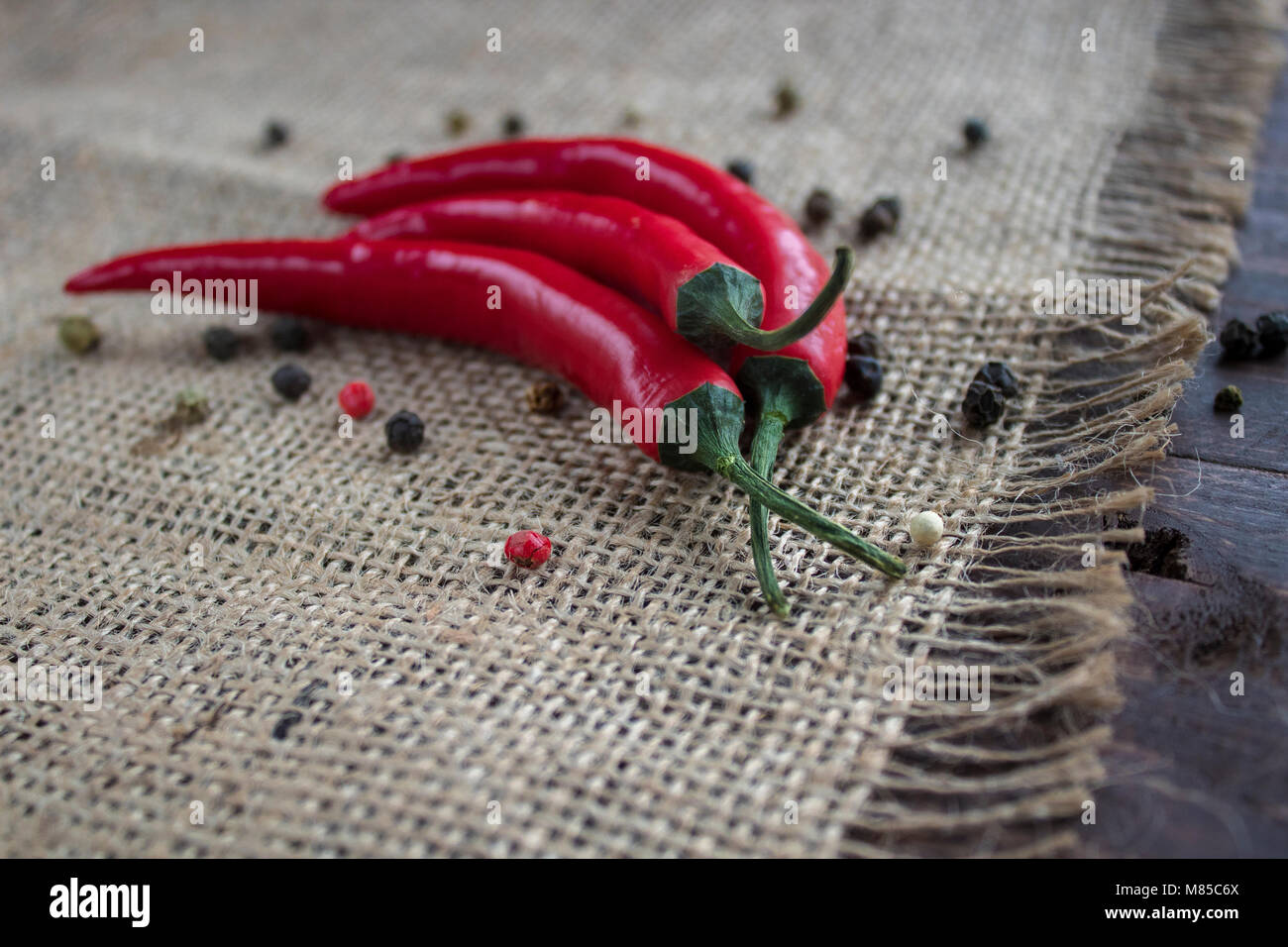 Chili pepper lies on a sackcloth on a wooden table. On the table scattered dry peppercorns Stock Photo