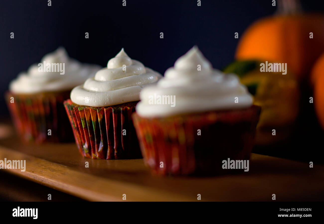 Delicious Pumpkin Spice Cupcakes with Cream Cheese Frosting with Pumpkins in the Background Stock Photo