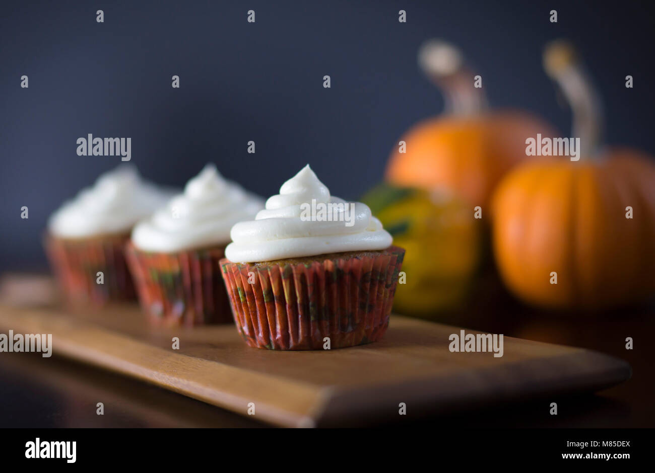 Delicious Pumpkin Spice Cupcakes with Cream Cheese Frosting with Pumpkins in the Background Stock Photo