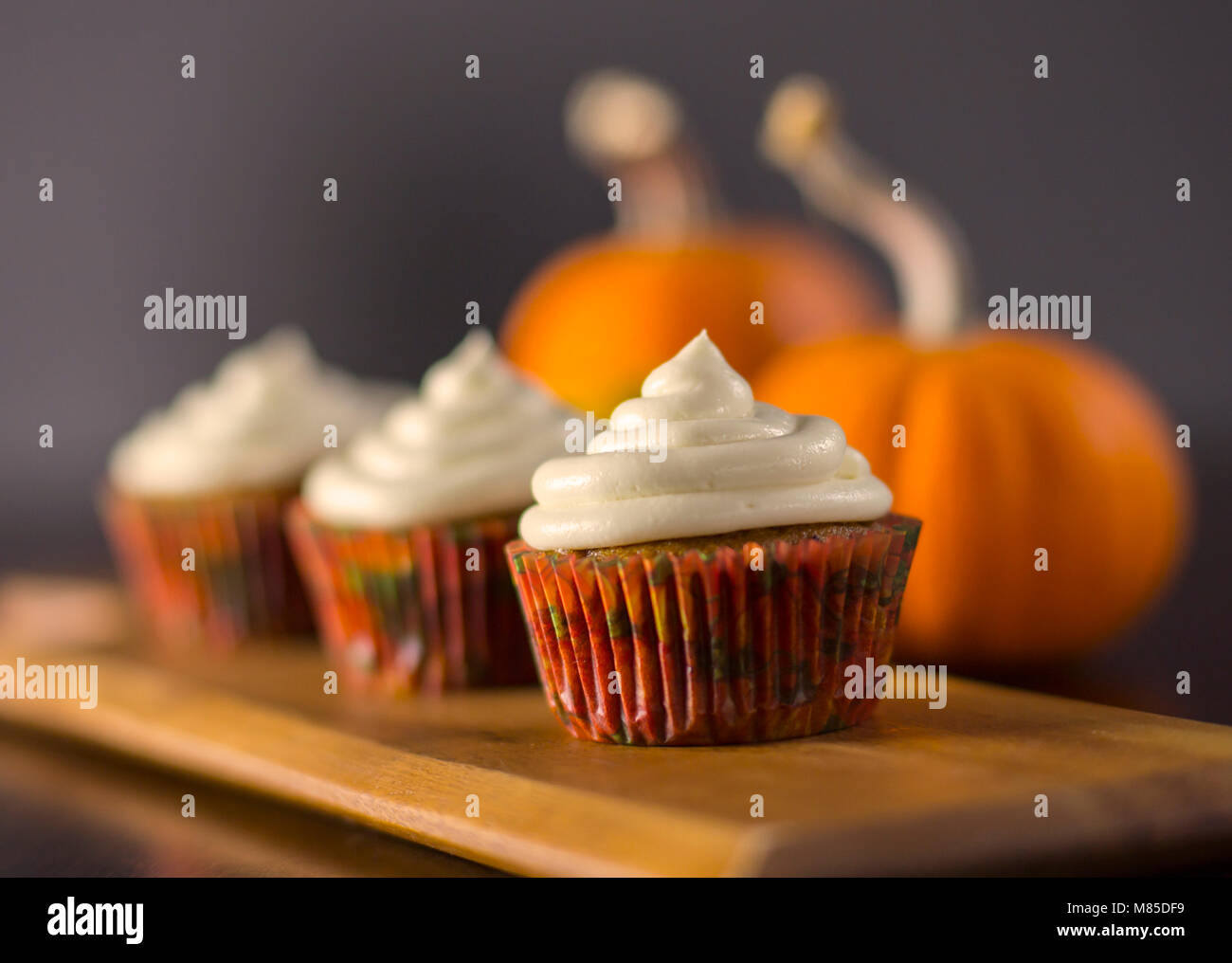 Delicious Pumpkin Spice Cupcakes with Cream Cheese Frosting with Pumpkins in the Background Stock Photo