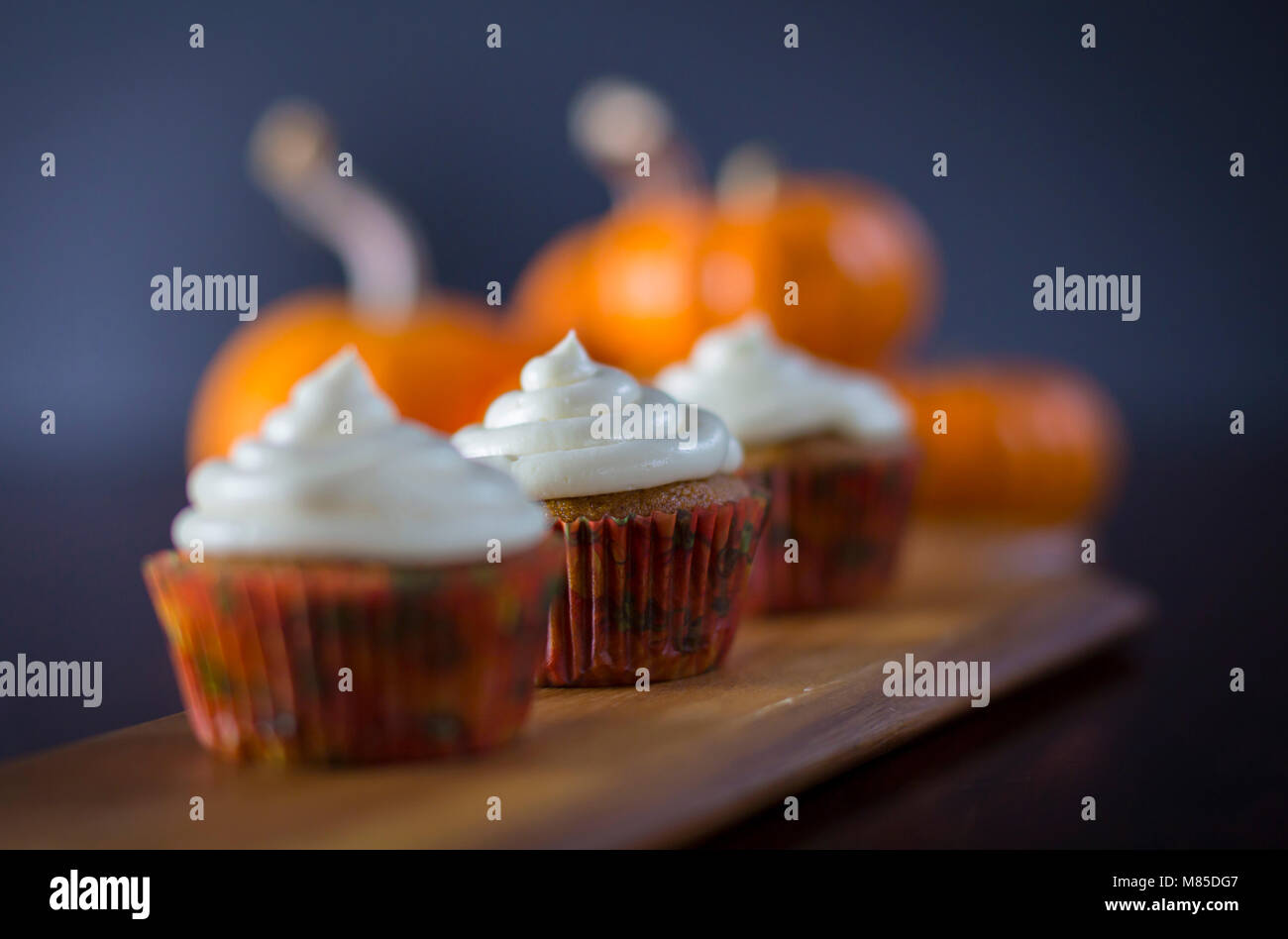 Delicious Pumpkin Spice Cupcakes with Cream Cheese Frosting with Pumpkins in the Background Stock Photo