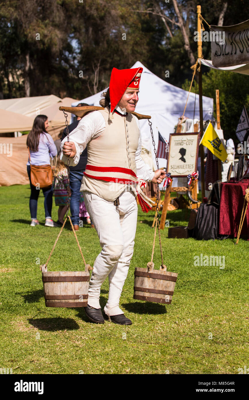 A man carrying a wooden yoke on his shoulders with barrels of water