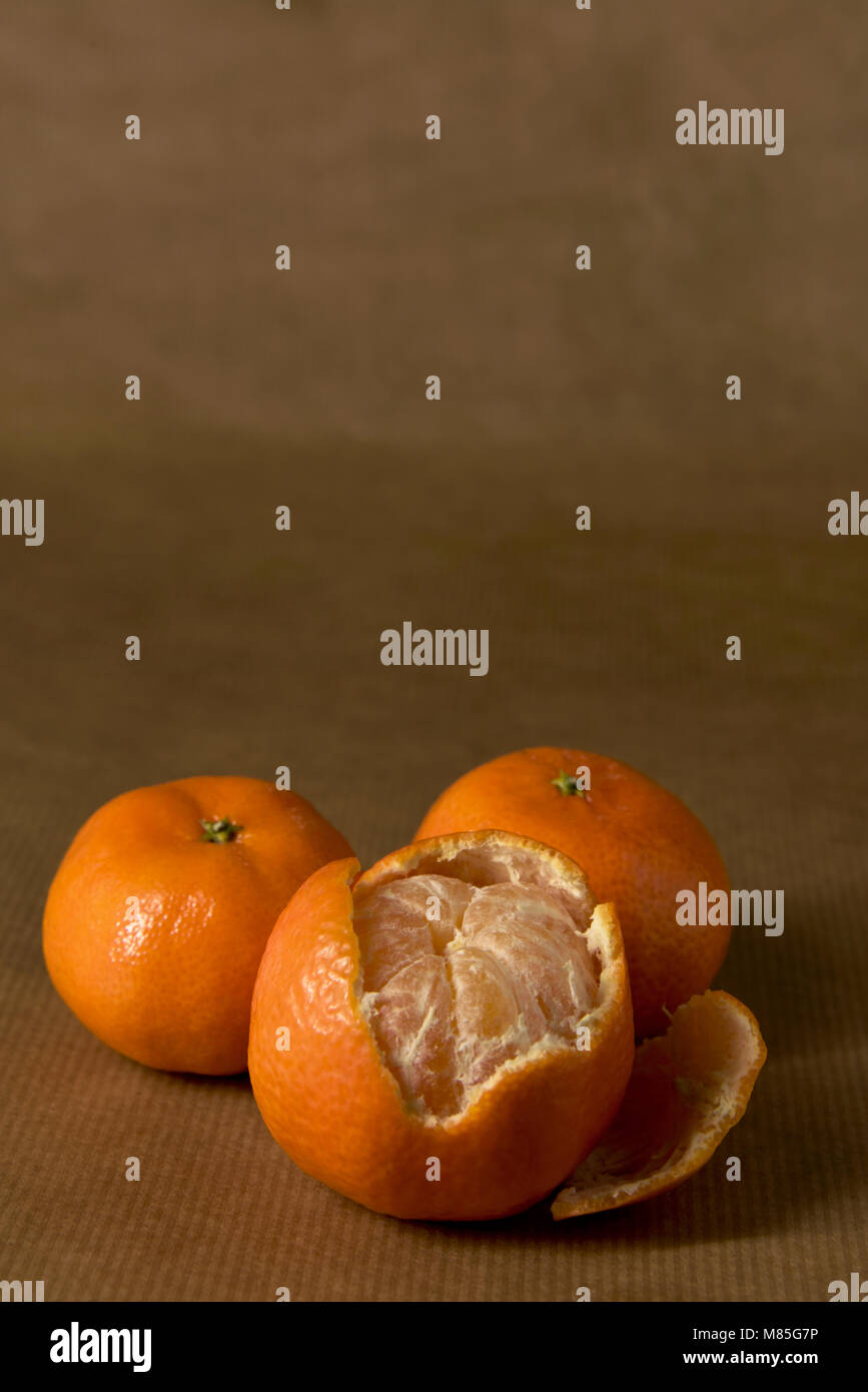 Three clementines, on halfpeeled on brown paper, with copy space
