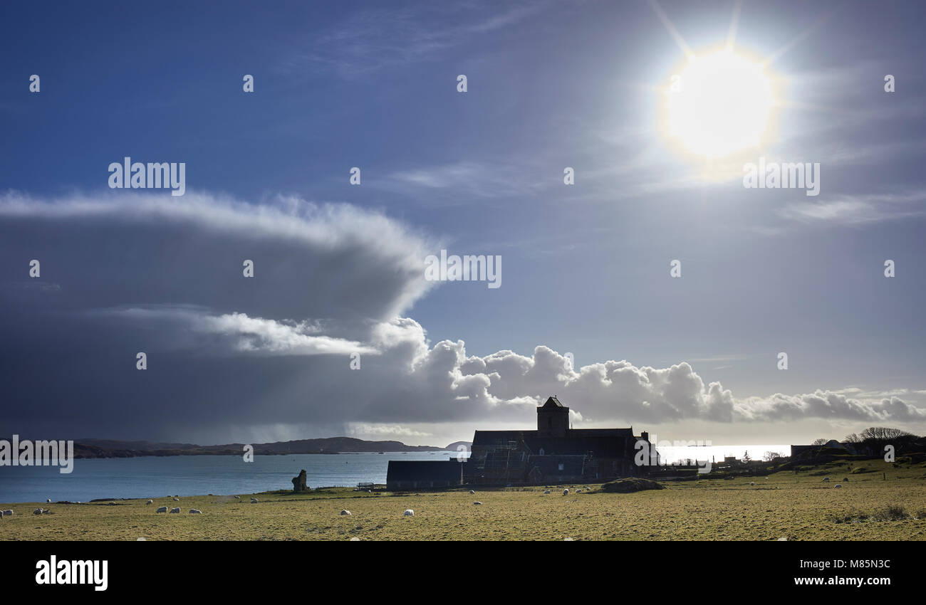 Lens flare highlights the view looking towards the South with stormy and rain soaked skies overlooking a silhouetted Abbey on Iona Stock Photo