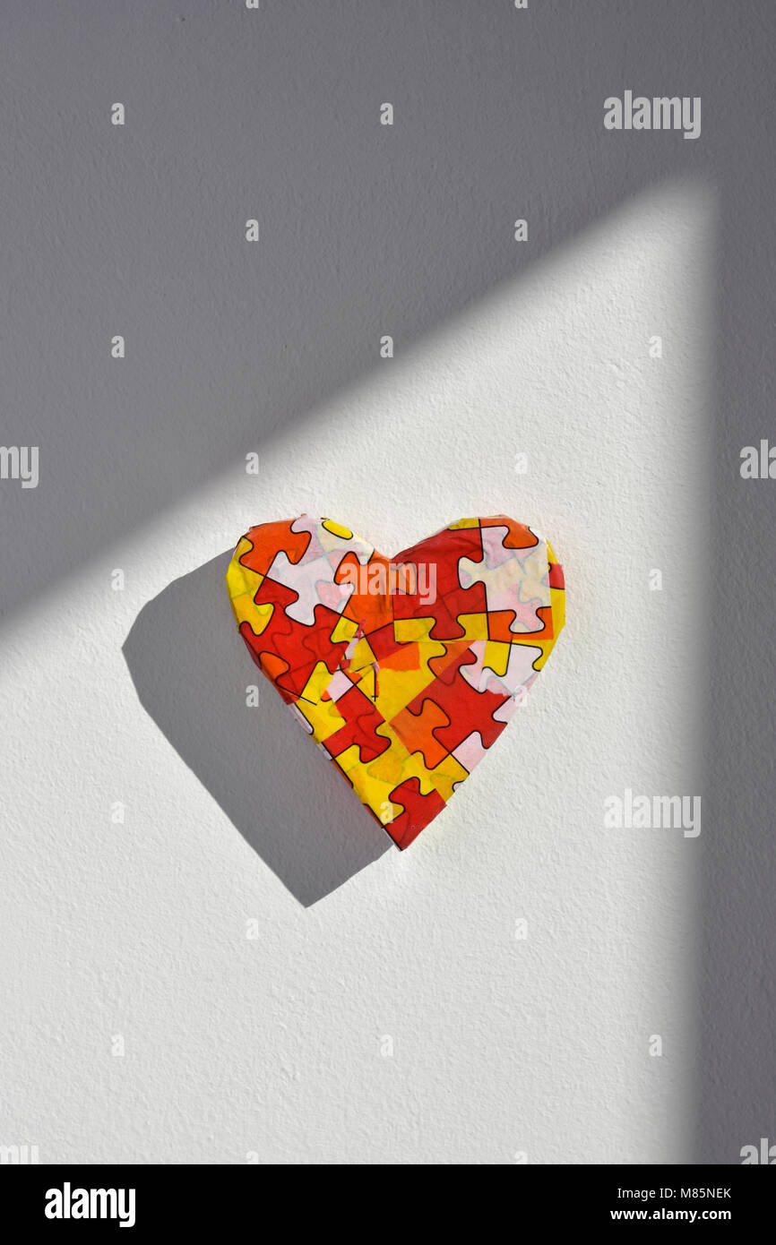 a heart patterned with many puzzle pieces of different colors, symbol of the autism awareness, on a white background Stock Photo