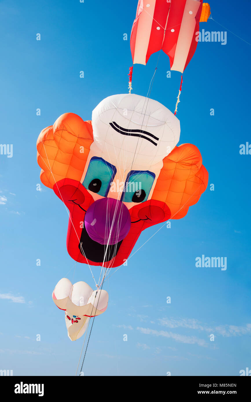 a kite in the shape of a clown face flying on the blue sky Stock Photo