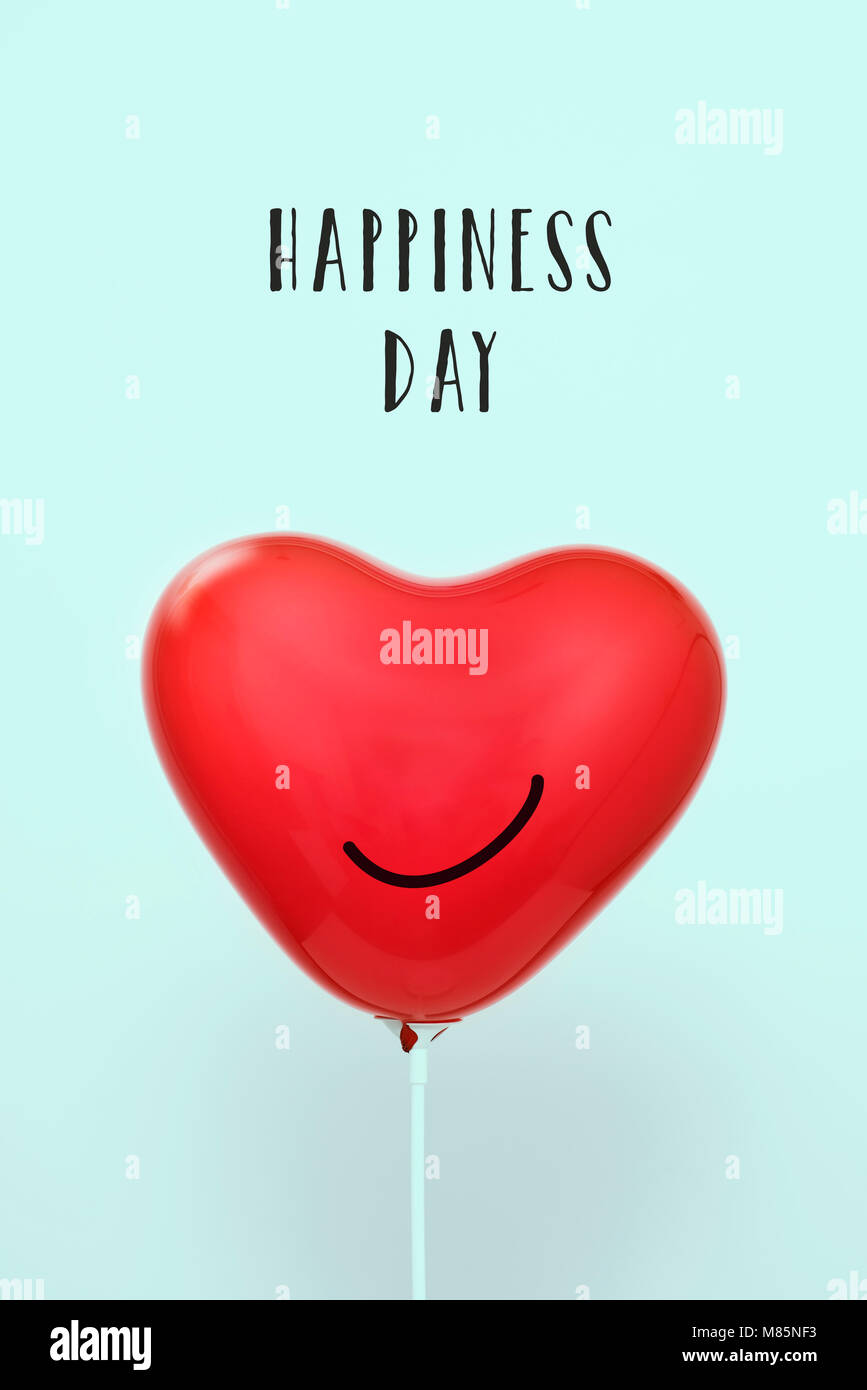 the text happiness day and a red heart-shaped balloon with a smile drawn in it, against a pale blue background Stock Photo