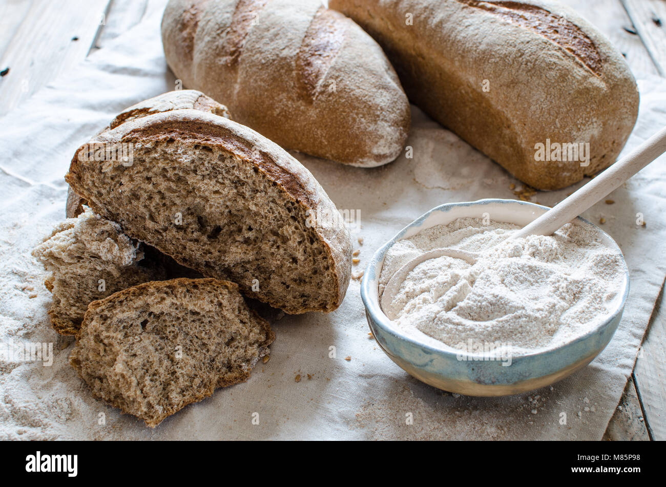 Whole grain bread  and flour on light background. Ceramic bowl full of whole grain flour Stock Photo