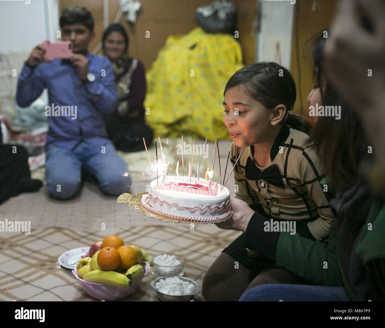 (180315) -- SARPOL-E ZAHAB, March 15, 2018 (Xinhua) -- Paria (R) blows out the candles on her birthday cake at her conex home in Sarpol-e Zahab, western Iran, on March 10, 2018. Paria, 10-year-old Iranian-Kurdish girl, lost her father during a 7.3-magnitude earthquake on Nov. 12, 2017. Now, she is living with her mother and only brother in a conex home, as their house was completely destroyed during the tremor. She has had her father as the 'hero' of her life, she sobbed. Asked what her top dream in her life is, she dropped her head saying in low voice: 'I cannot think of another disaster like Stock Photo