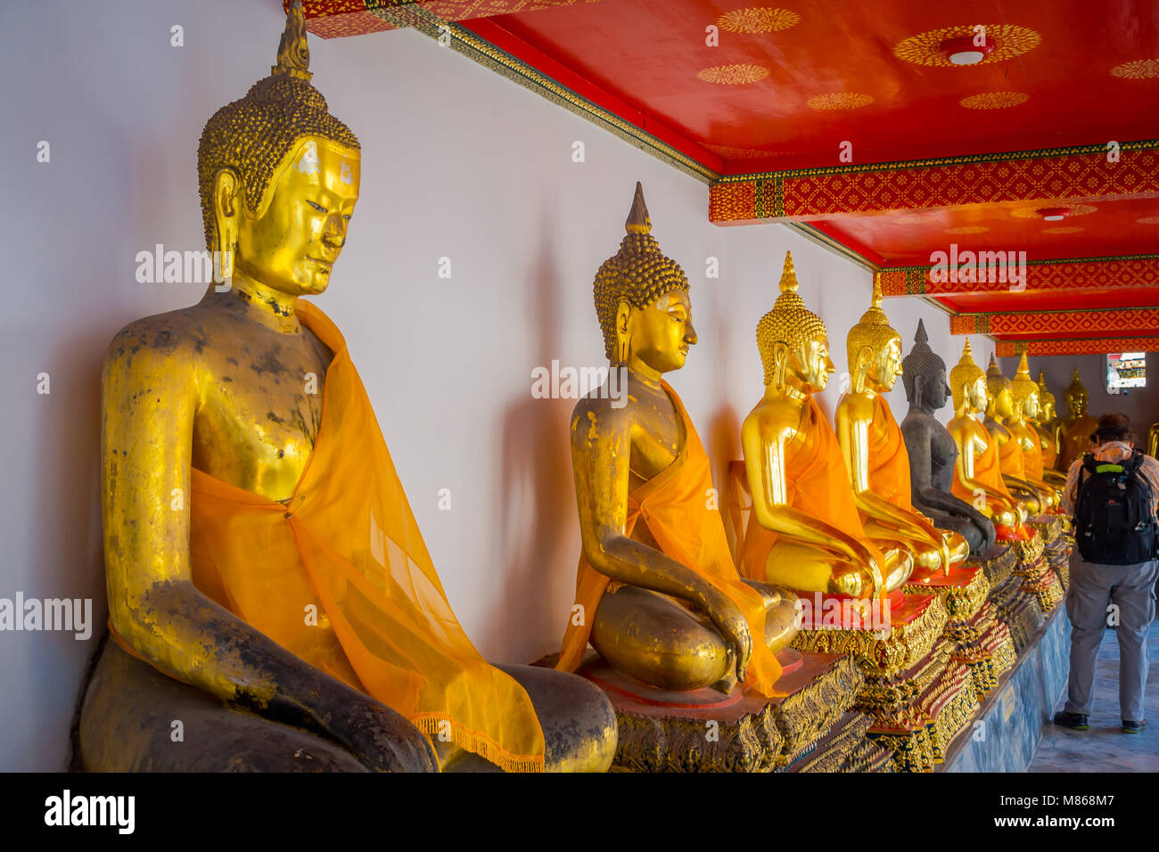 BANGKOK, THAILAND, FEBRUARY 08, 2018: Indoor view of unidentified people close to a golden Buddha Statues in a row in Wat Pho Temple in Thailand Stock Photo