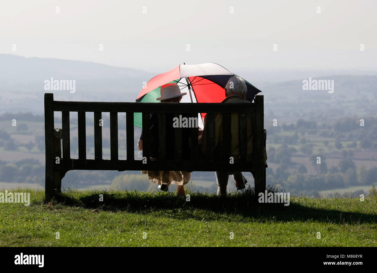 Couple sat, sheltering under an umbrella in Autumnal sunshine. Worcestershire, September Stock Photo