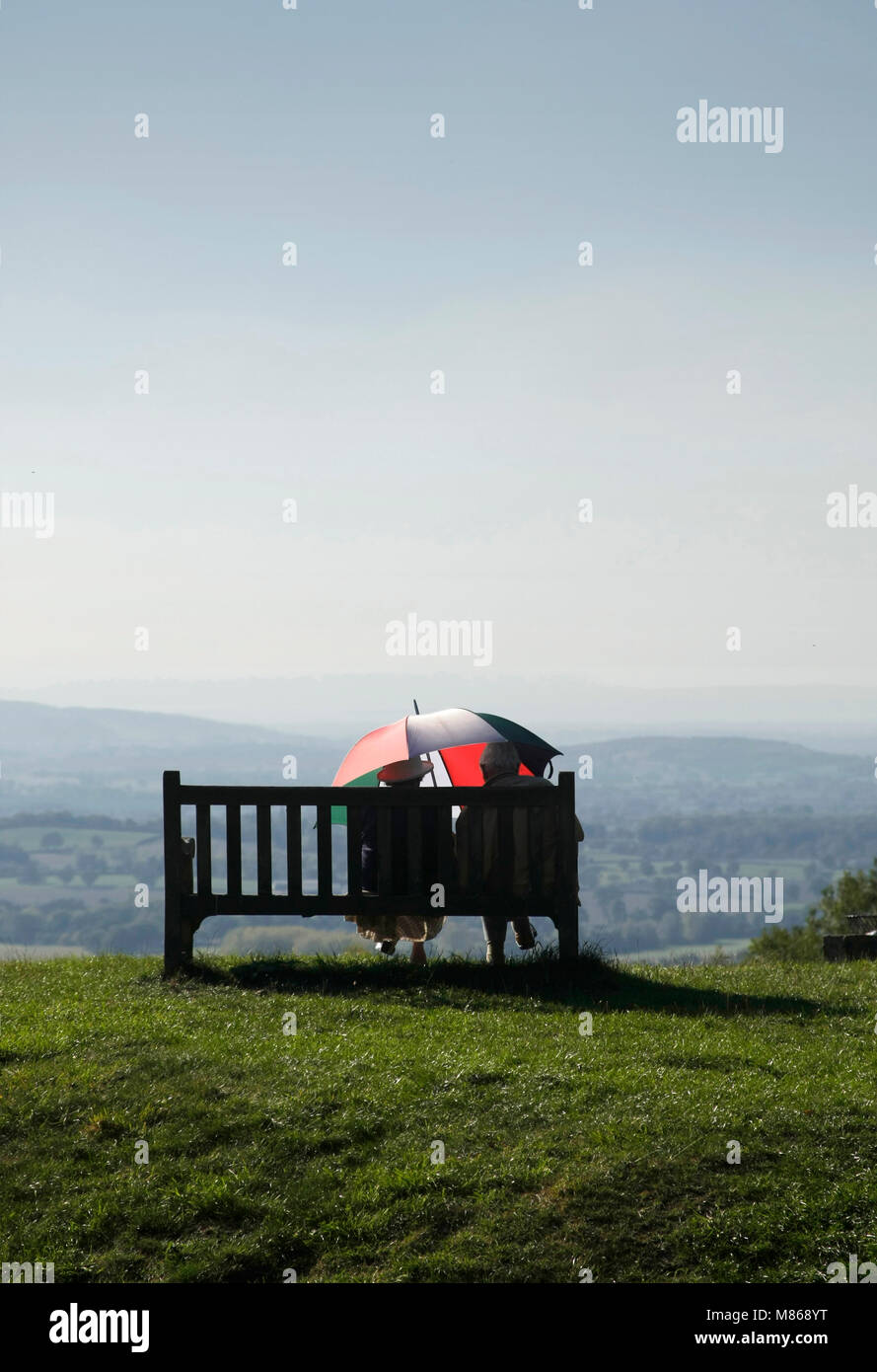 Couple sat, sheltering under an umbrella in Autumnal sunshine. Worcestershire, September Stock Photo