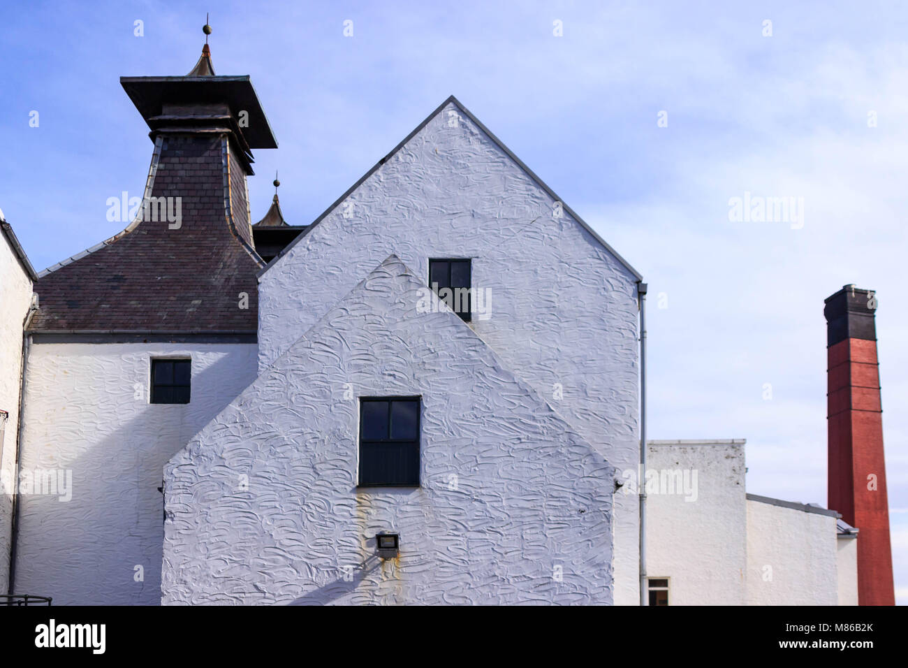 White brick buildings with cupola rooftop and a red smoke stack at a Scotch Distillery on the island of Islay, Scotland, UK Stock Photo