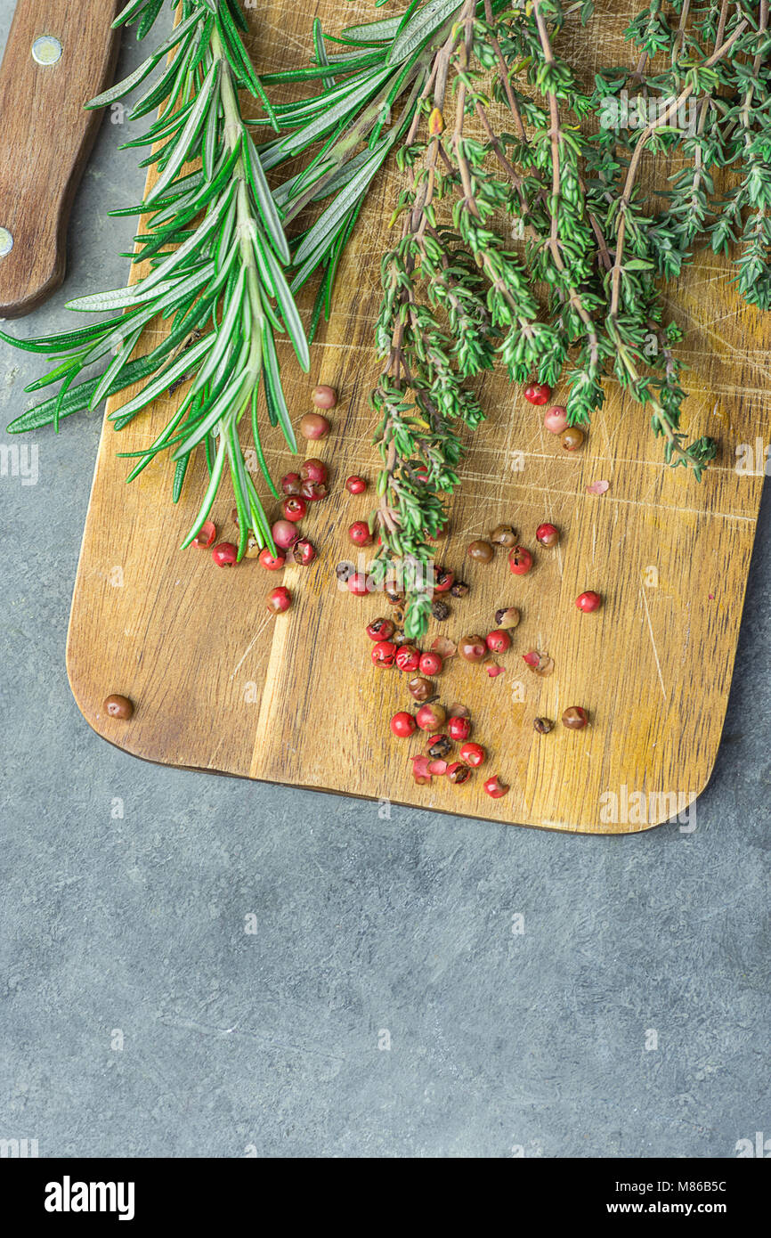 Fresh Provence Herbs Rosemary Thyme Twigs red Pink Peppers on Aged Wood Cutting Board Knife on Dark Concrete Stone Table. Top View. Mediterranean Cuis Stock Photo