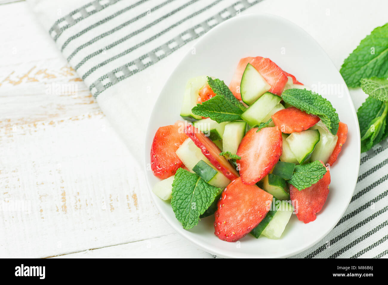 Fresh Detox Summer Spring Salad with Strawberries Green Mint Leaves in White Ceramic Bowl on Cotton Kitchen Towel. Plank Wood Table. Top View. Clean E Stock Photo