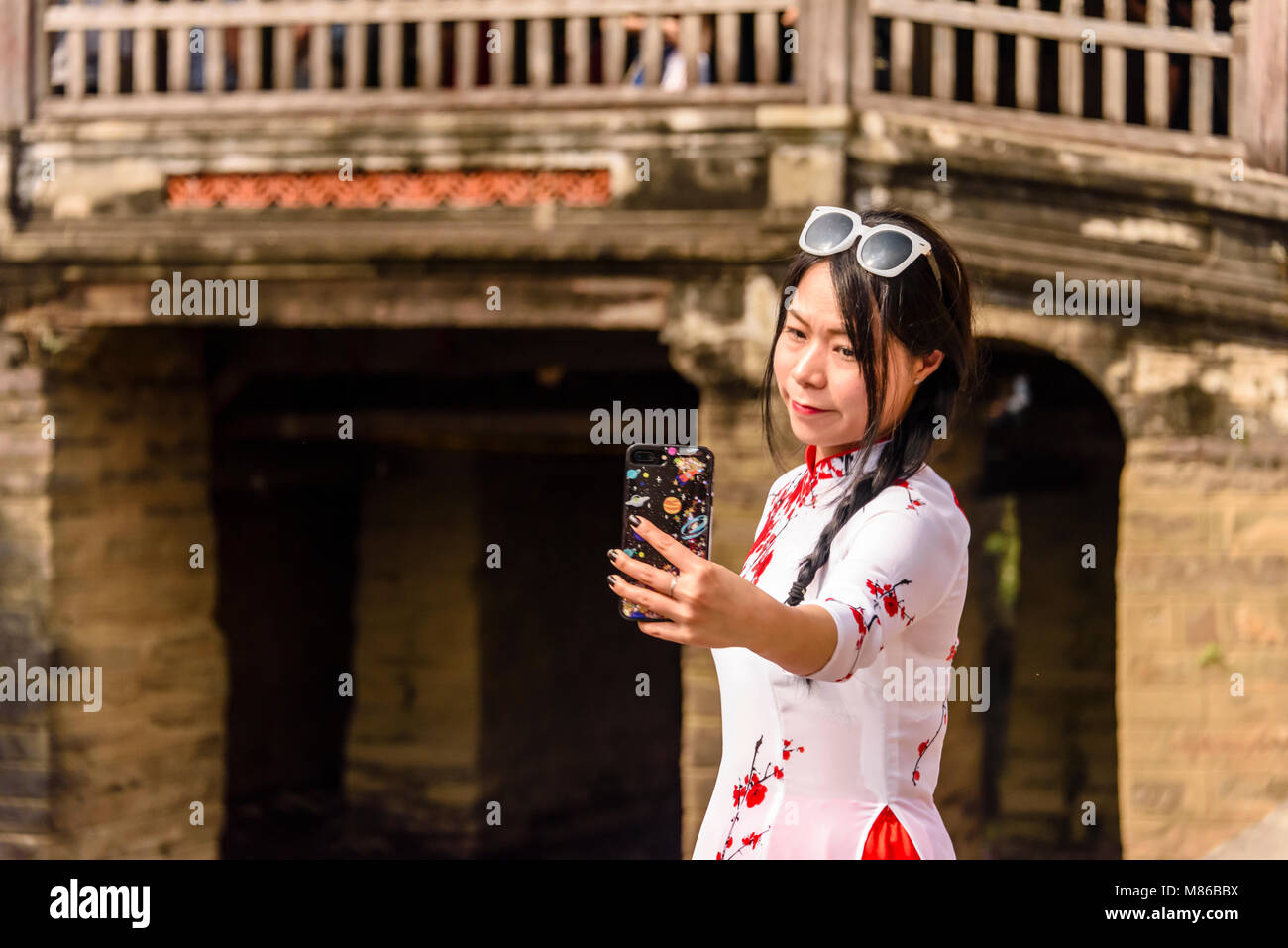 A woman takes a selfie at the Chùa Cầu Japanese bridge, an 18th century carved wooden bridge which incorporates a shrine, in Hoi An, Vietnam Stock Photo