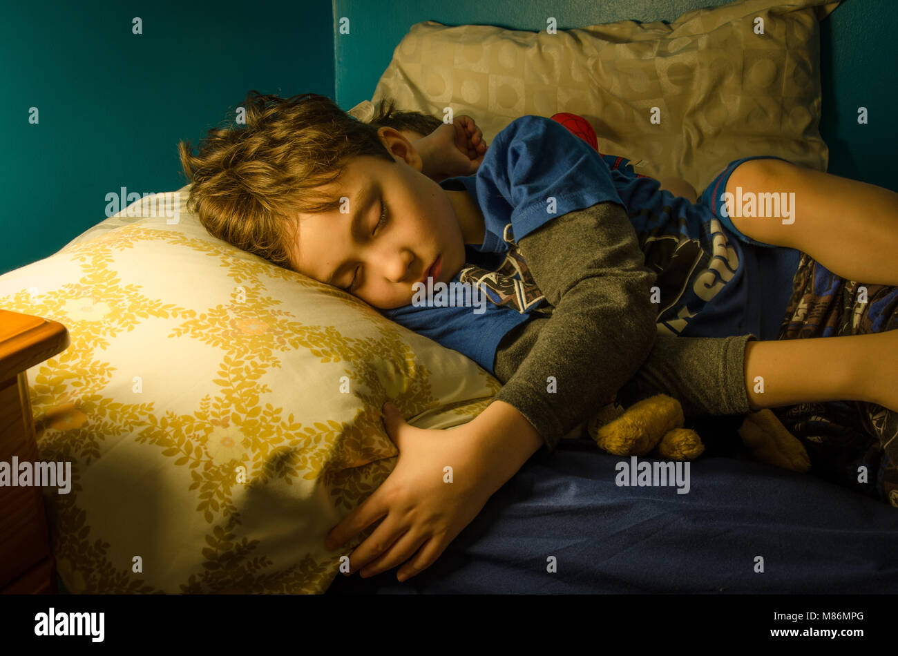 Two young brothers asleep in the same bed at nighttime. The scene is