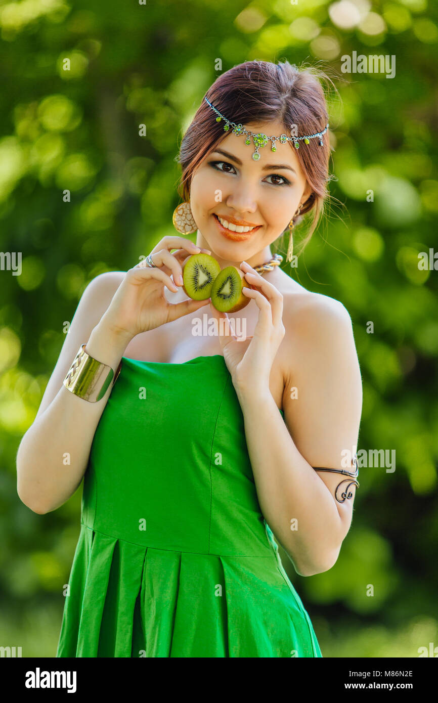 Portrait of a beautiful young asian woman holding two halves of kiwi ...